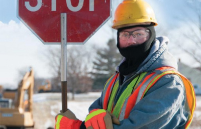 A worker in safety gear holding a stop sign and wearing a neck gator