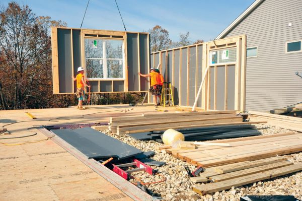 Two men in bright orange t-shirts and hard hats installing wall panels on a residential home